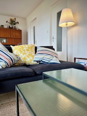 A modern living room with a dark sofa, striped and patterned cushions, a glass coffee table, and a floor lamp. - Family vacation home facing the beach on the edge of the GR34 (Porspoder)