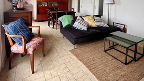 A living room with a sofa, chairs, a coffee table, and a kitchen area in the background. - Family vacation home facing the beach on the edge of the GR34 (Porspoder)