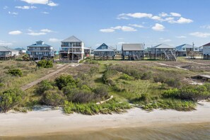A coastal residential area with houses on stilts, a sandy beach, and a clear sky. - Waterfront Home with Private Sound Access & Walk to Gulf Beaches (Dauphin Island)
