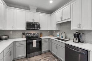 A modern kitchen with white cabinets, stainless steel appliances, and a white countertop. - Spacious canal-front home, walk to Gulf beaches, sleeps 16 (Dauphin Island)