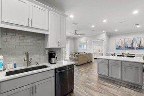 A modern kitchen with white cabinets, a dishwasher, and a coffee maker. - Spacious canal-front home, walk to Gulf beaches, sleeps 16 (Dauphin Island)