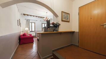 A hallway with a red sofa, a small table with a lamp, a wooden door, and a framed picture on the wall.