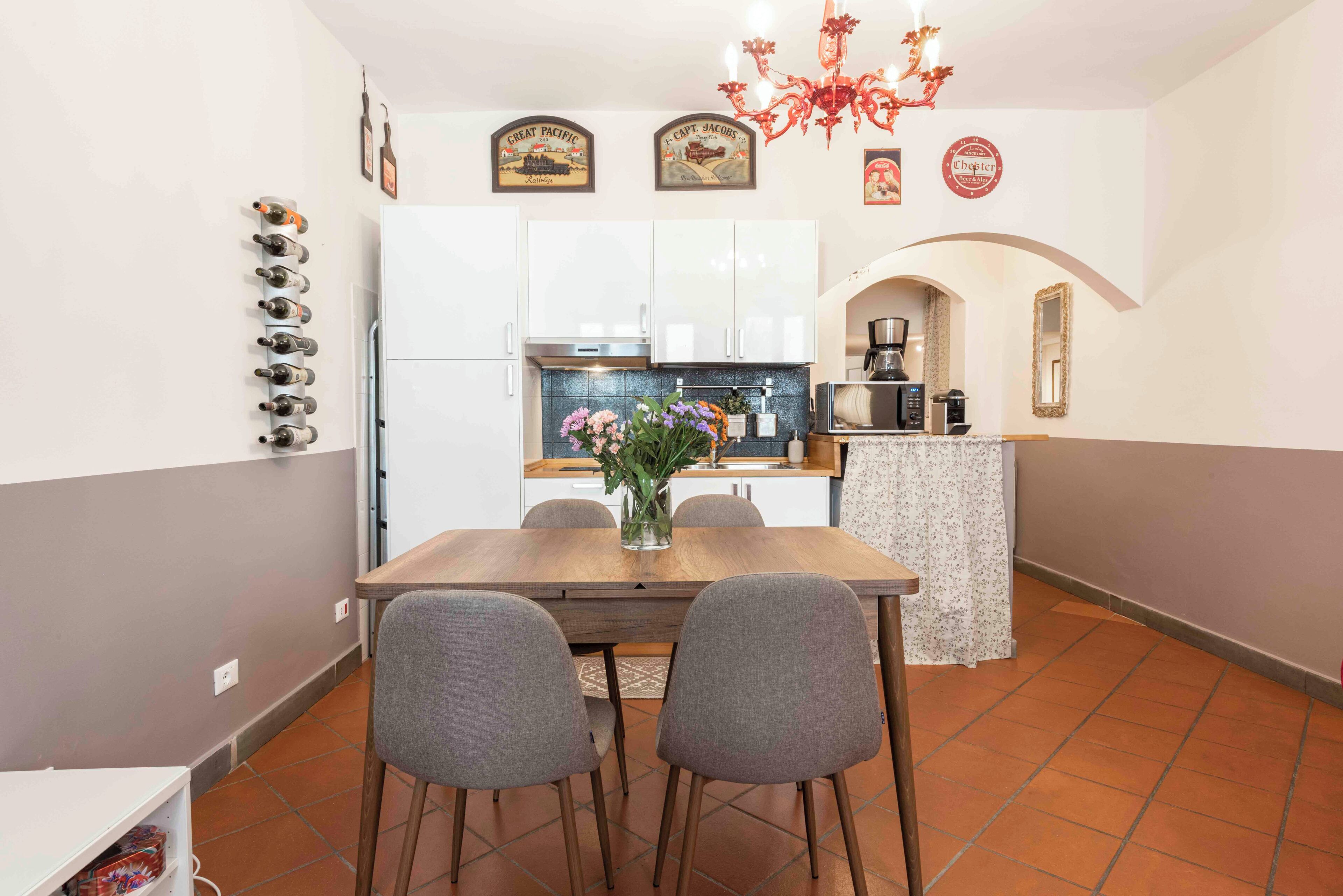 Une cuisine compacte avec des meubles blancs, une table à manger avec quatre chaises et un petit îlot central doté d’une machine à café.