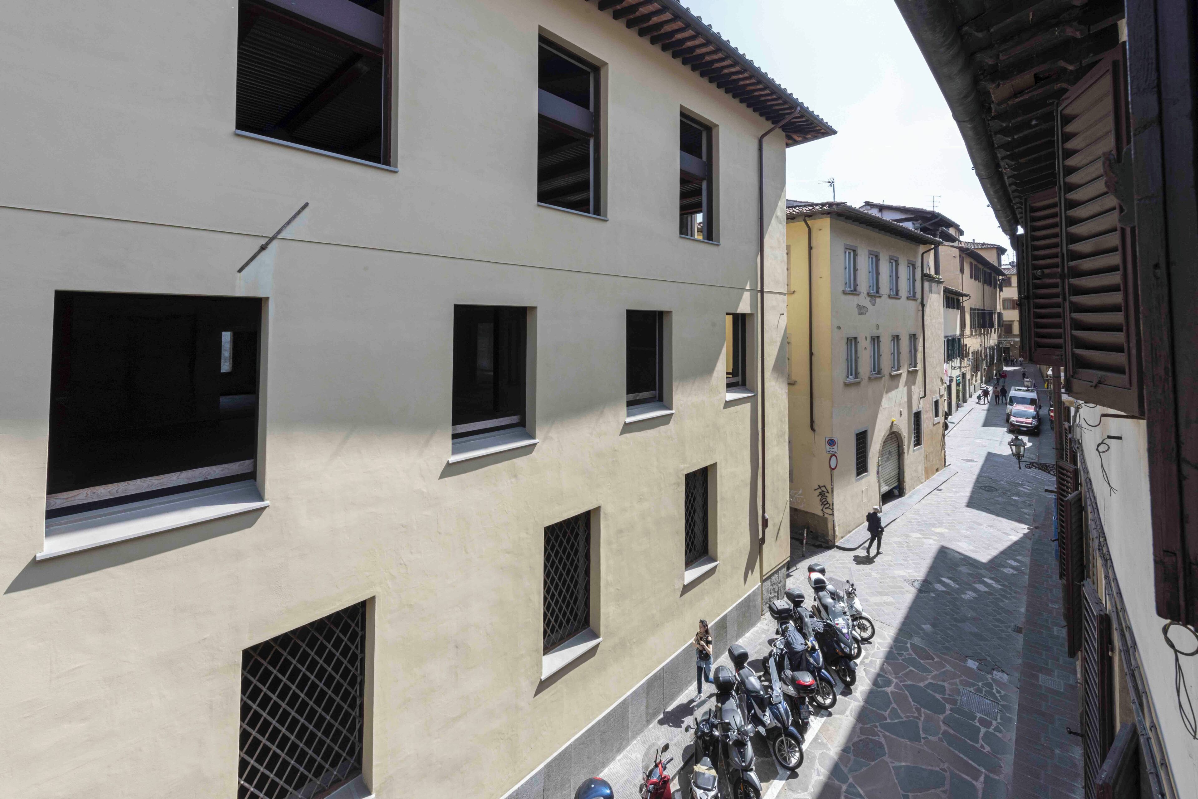 A narrow street with buildings on either side, a row of parked motorcycles, and a person walking.