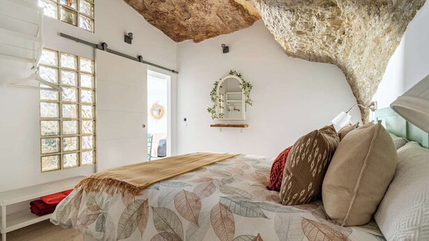 Een slaapkamer met een groot bed, een bankje, een raam met uitzicht en een bijzondere plafondconstructie.
