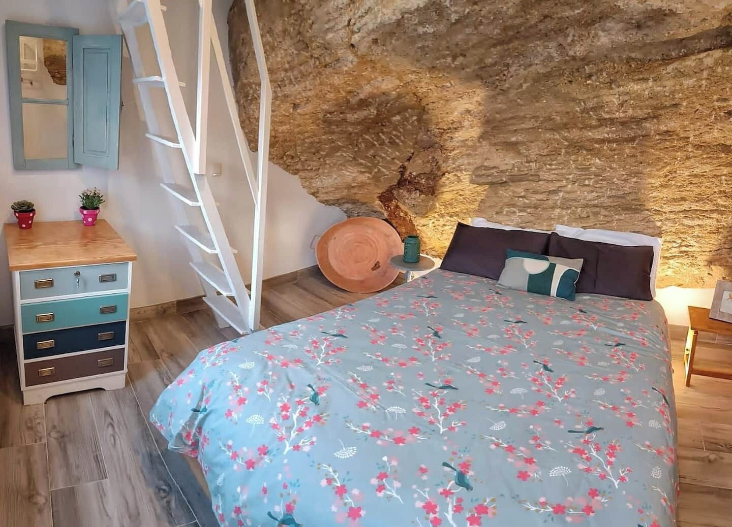 Ein Schlafzimmer mit Bett, Schminktisch und einer Leiter, die an einer Steinsäule lehnt.