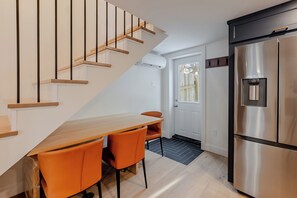 Eine moderne Küche mit einer Holztreppe, einem Edelstahlkühlschrank und einem Essbereich mit orangefarbenen Stühlen.