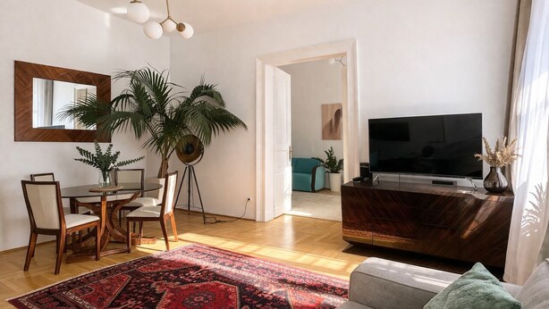A living room with a sofa, a TV, a dining table with chairs, a red patterned rug, and a potted plant. - AVATAR Suite (Budapest)