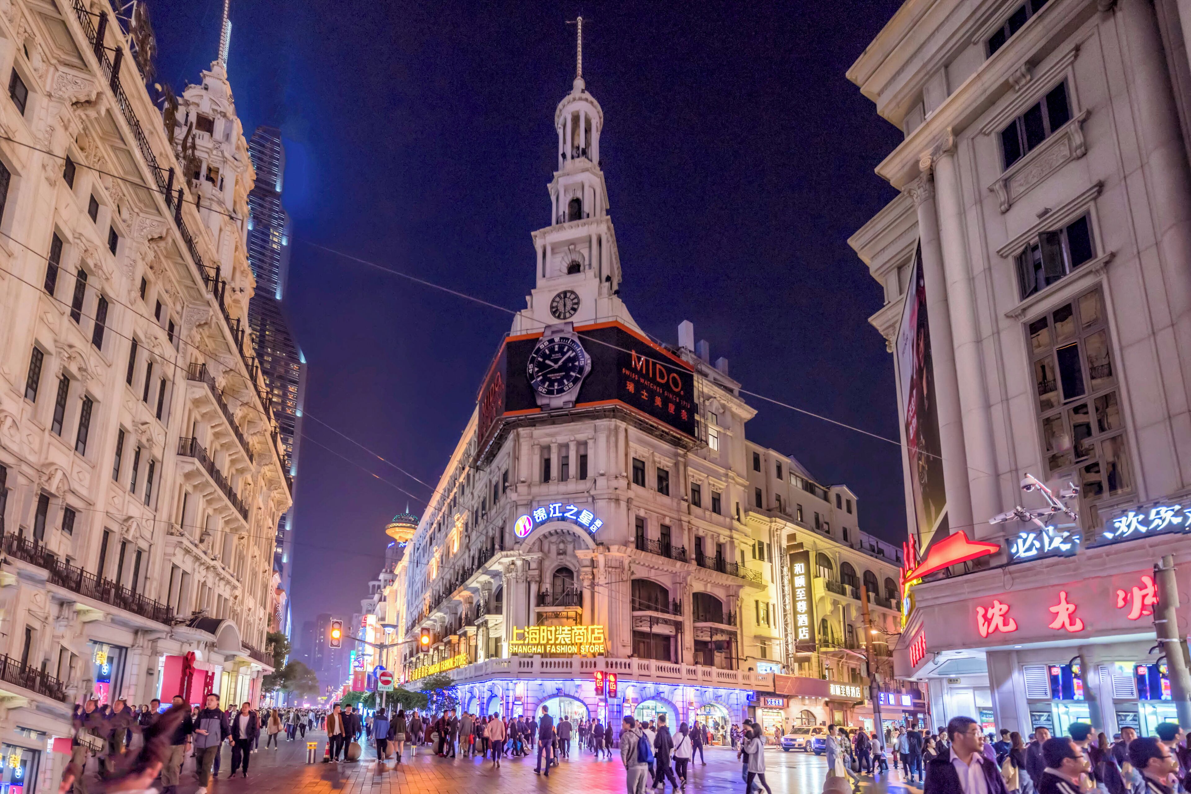 A historic building with a clock tower, a prominent sign for a fashion store, and a bustling street scene.