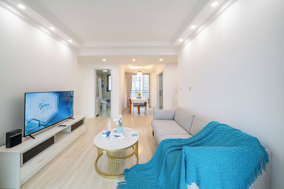 Una sala de estar moderna con un televisor de pantalla plana, un sofá, una mesa de centro y un comedor al fondo.