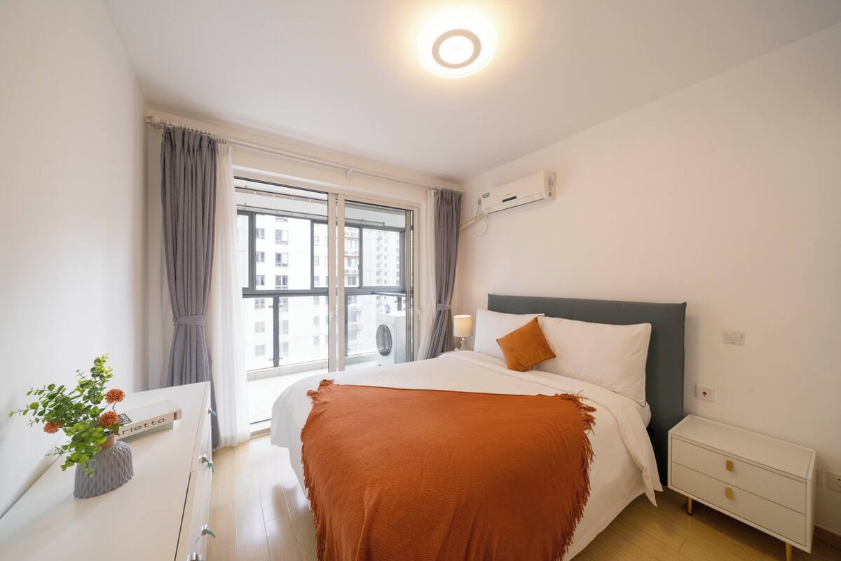 Una habitación de hotel moderna con una cama grande, una mesita de noche y un ventanal con cortinas.