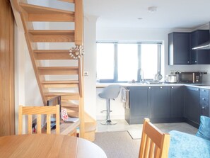 A modern kitchen with dark cabinets, a microwave, and a coffee maker. There's a wooden staircase leading to another level.
