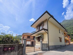 A two-story building with a balcony, a gated entrance, and a mountainous backdrop. - Cosy apartment for 5 guests with WIFI, TV and terrace (Premosello-chiovenda)