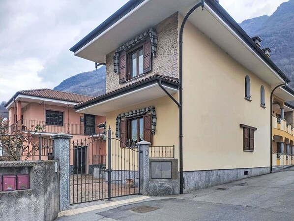 A two-story building with a balcony, a stone wall, and a metal gate. - Cosy apartment for 5 guests with WIFI, TV and terrace (Premosello-chiovenda)