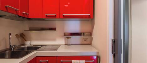A kitchen with red cabinets, a stainless steel sink, and a towel hanging on the door.