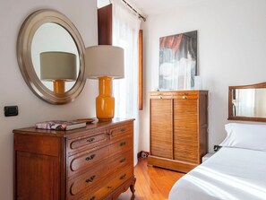 Ein Schlafzimmer mit einem hölzernen Schminktisch, einem Bett, einem Kleiderschrank, einem runden Spiegel und einem Bild an der Wand.