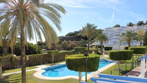 Ein Pool, umgeben von ordentlich geschnittenen Hecken und Palmen, mit einem Gebäude im Hintergrund.