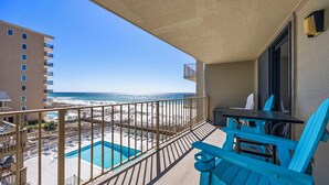 Un balcón con vista a la playa, una piscina y una mesa con sillas.