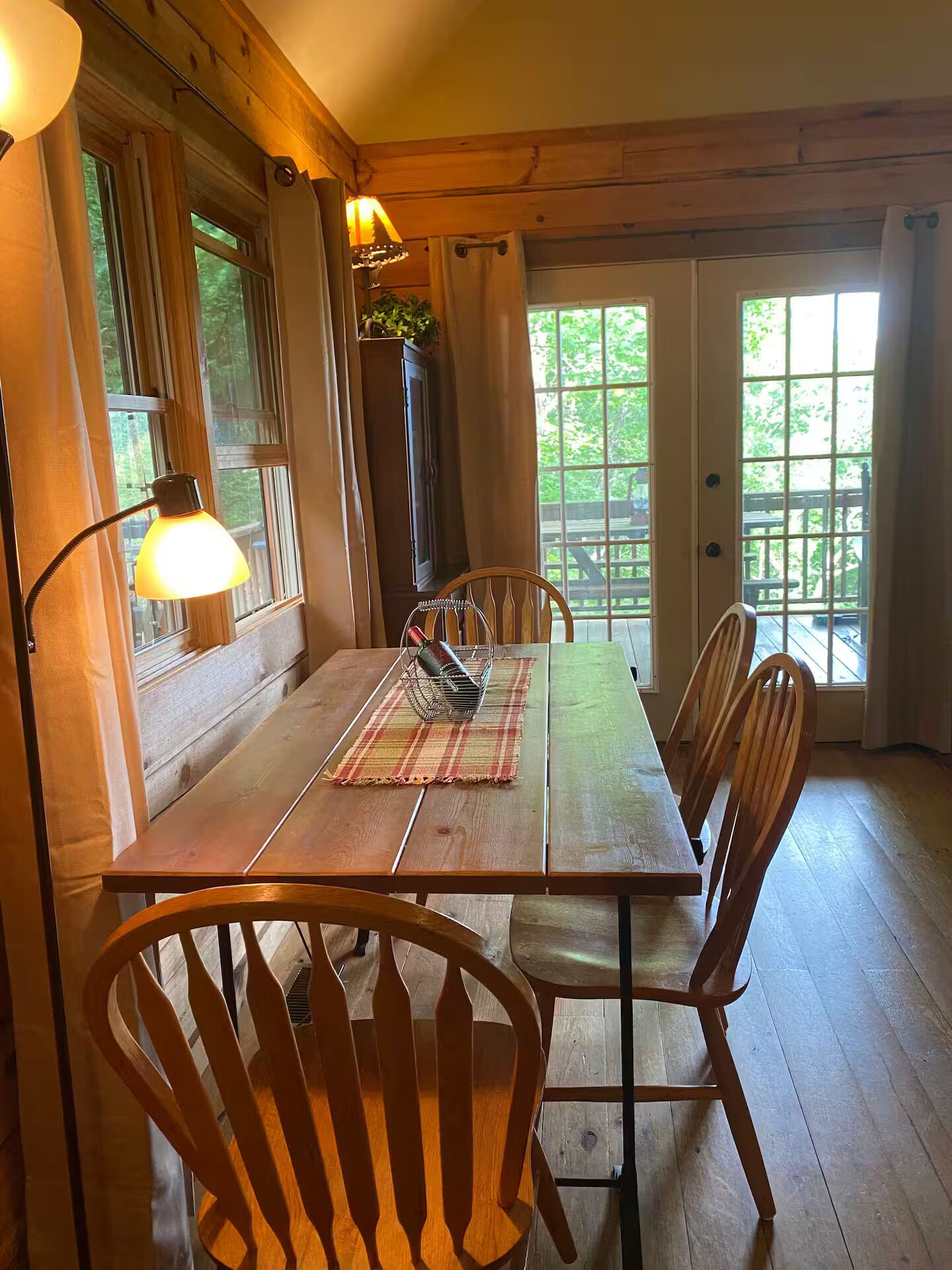 A wooden dining table with chairs, a lamp, and a window with curtains.