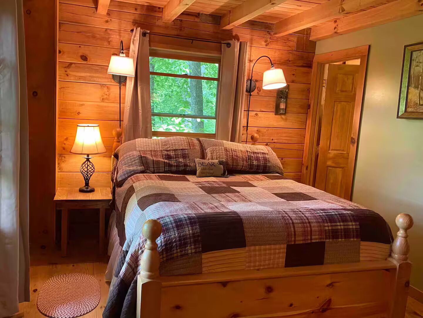 A wooden cabin bedroom with a bed, two bedside lamps, a window, and a door.