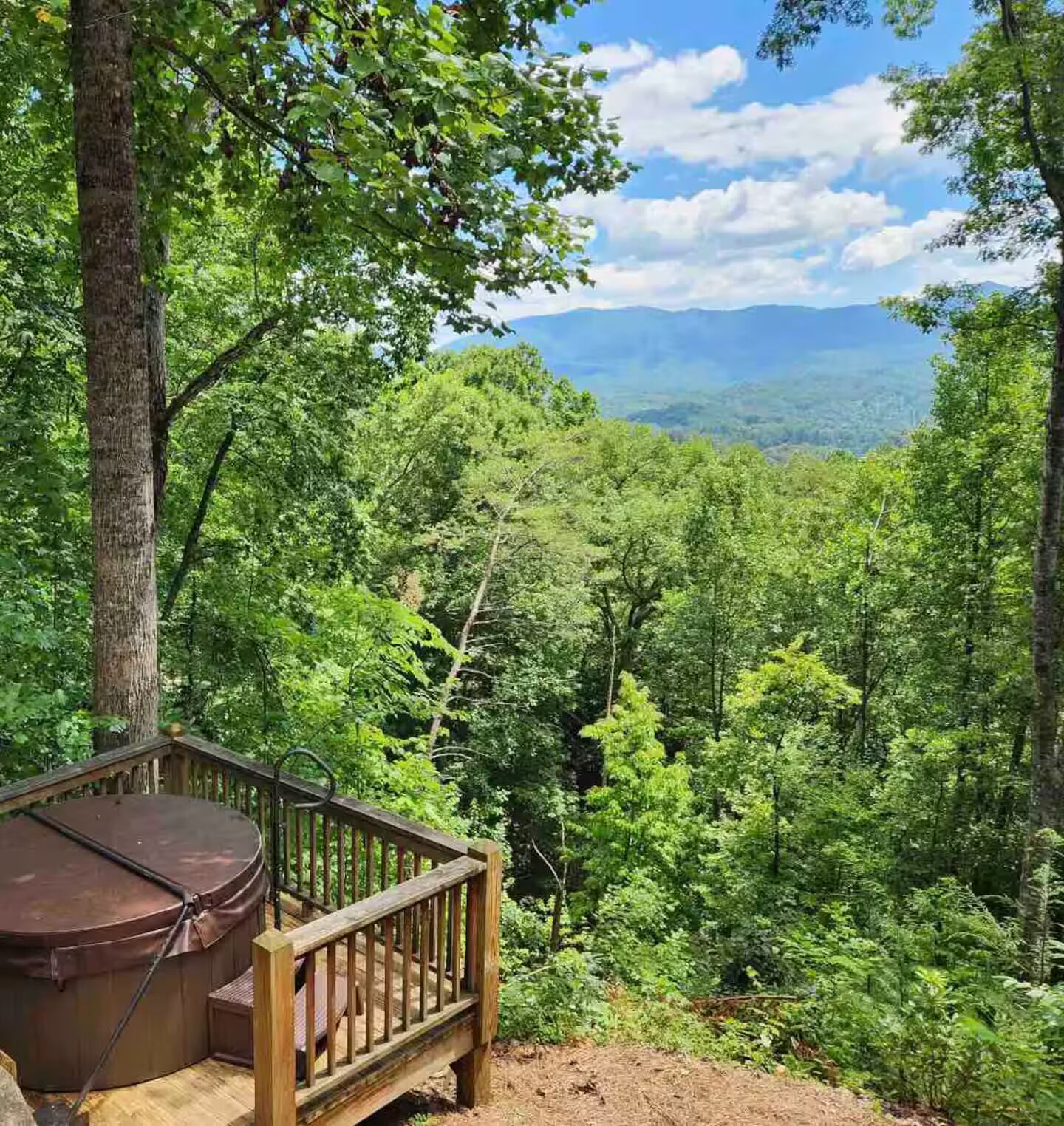 A wooden deck with a hot tub, surrounded by dense forest and a mountain view.