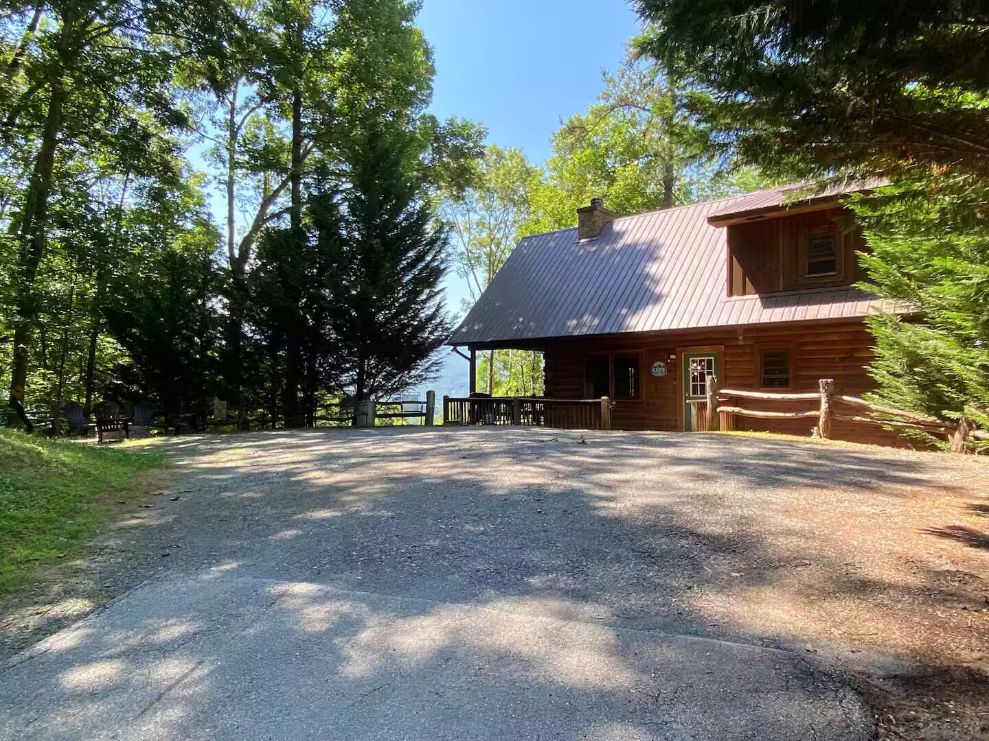 A rustic cabin with a metal roof, surrounded by tall trees and a gravel driveway.