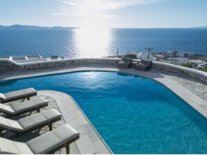 Una piscina con sillas de descanso, un muro de piedra y vistas al mar.