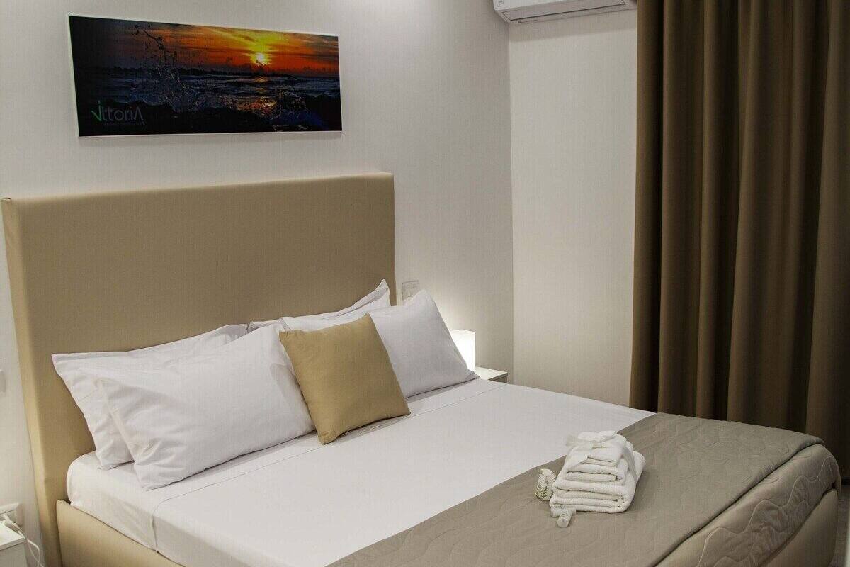 A hotel room with a bed, a painting, an air conditioner, and a curtain.