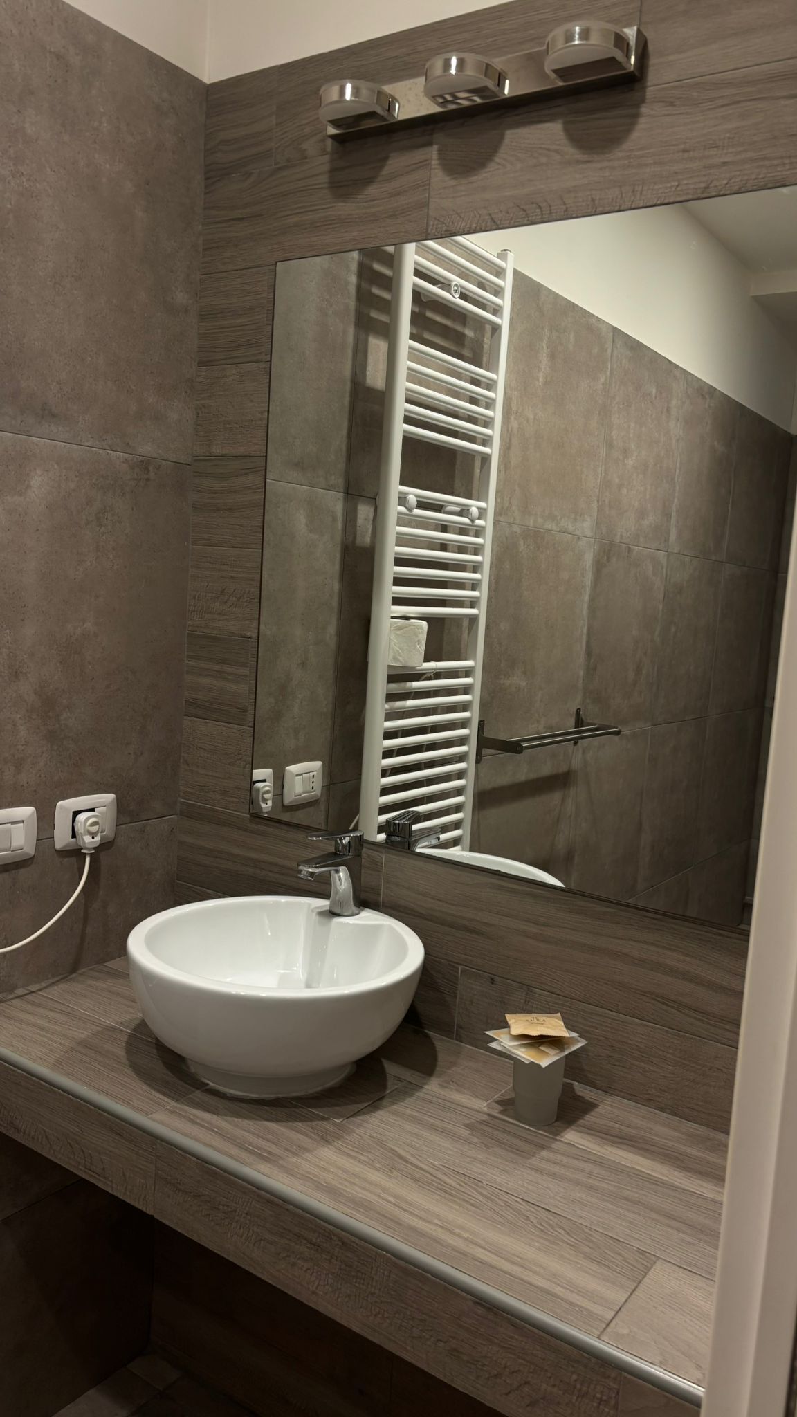 A bathroom with a large mirror, a white sink, and a towel rack.