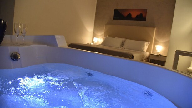 A room with a bathtub, a bed, and two bedside tables with lamps. - Favorite Room&Spa (San Giuseppe Vesuviano)