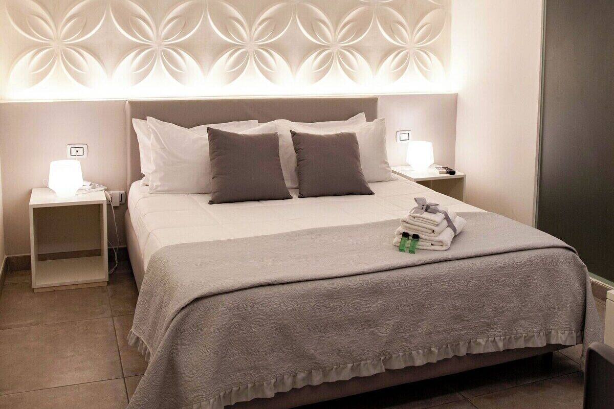 A modern hotel room with a large bed, two bedside tables, a wall with a geometric pattern, and a large mirror.