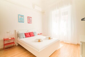 A bright hotel room with a bed, a nightstand, a red shelf, and two framed pictures on the wall. - Gloria s Nest 5 Minutes to Porta Romana (Milan)