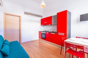 A modern kitchen with red cabinets, a white countertop, and a dining area with red chairs. - Gloria s Nest 5 Minutes to Porta Romana (Milan)
