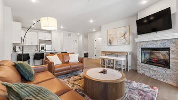 Een moderne woonkamer met een leren bank, een ronde salontafel, een open haard en een flatscreen televisie erboven.