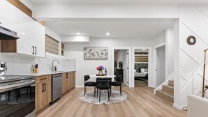 A modern kitchen with a dining area, wooden cabinets, and a staircase. - 2BR Near YEG Airport | King Bed + Mini Golf! (Nisku)