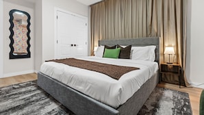 A bedroom with a bed, a nightstand, a lamp, a door, and a mirror. - 2BR Near YEG Airport | King Bed + Mini Golf! (Nisku)