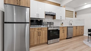 A modern kitchen with stainless steel appliances, wooden cabinets, and a marble backsplash. - 2BR Near YEG Airport | King Bed + Mini Golf! (Nisku)
