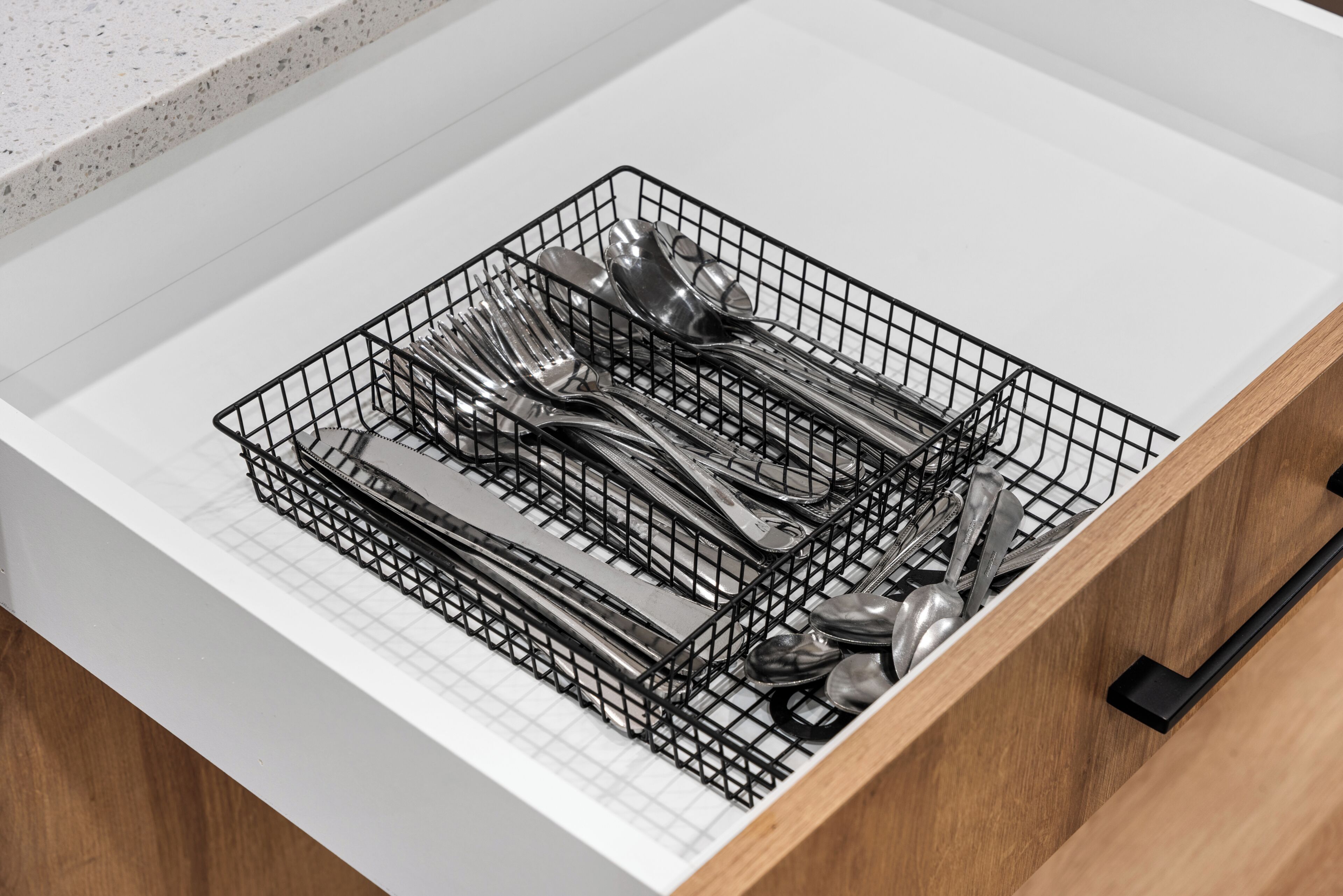 En låda med ett svart metallfack för att organisera bestick, innehållande gafflar, knivar och skedar.
