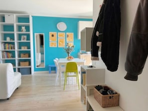 Ein modernes Wohnzimmer mit einem weißen Sofa, einem grünen Sessel, einem Esstisch und einem Bücherregal.