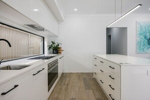 A modern kitchen with white cabinetry, a built-in oven, a stainless steel sink, and a wooden floor.