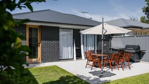 Eine Terrasse mit Tisch, Stühlen, einem Grill und einer Schiebetür.