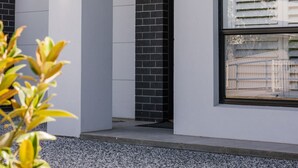 Ein modernes Gebäude mit weißer Fassade, einer Ziegel-Säule und einem Fenster mit horizontalen Rollläden.