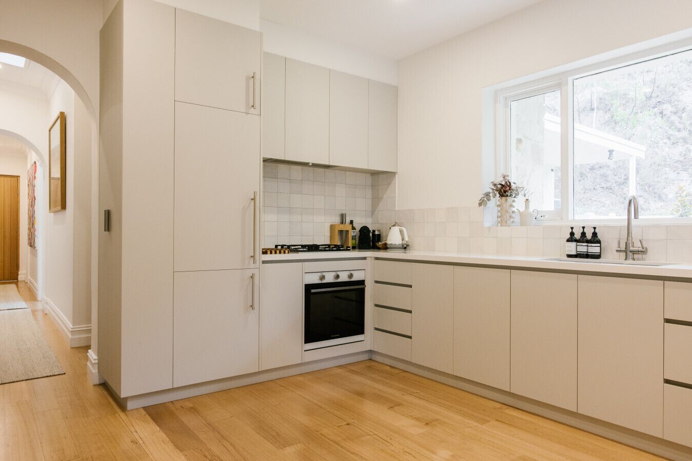 A modern kitchen with white cabinetry, a built-in oven, and a window above the sink.