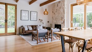 A spacious living room with a wooden floor, a stone fireplace, a wooden ceiling, and a large window.