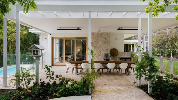 A covered patio with a dining area, stone wall, and a view of a pool.
