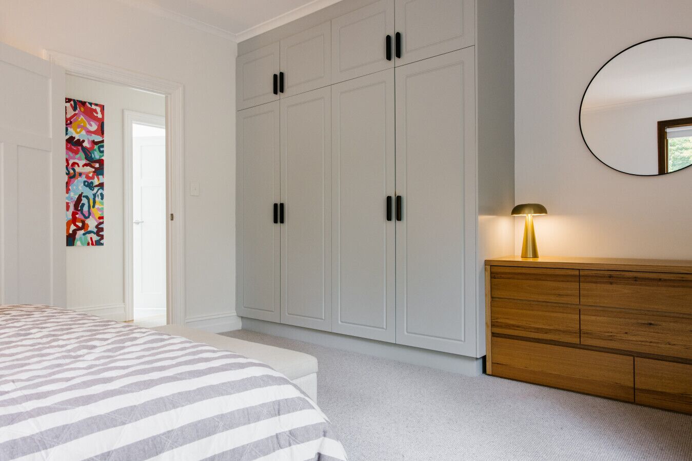 Une chambre à coucher comprenant un lit, une armoire, une commode et une lampe fixée au mur.