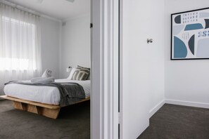 A bedroom with a bed, a bedside table, a wall-mounted light, and a framed abstract artwork. - 2BR Gem Apartment Near Henley Beach South (Henley Beach South)
