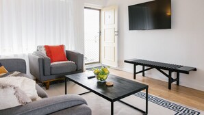 Een moderne woonkamer met een grijze bank, een salontafel met een bloevas, een zwarte bank en een aan de muur bevestigde televisie.