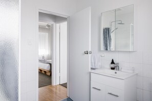 Ein modernes Badezimmer mit Waschbecken, Spiegel und Dusche, alles in Weiß.