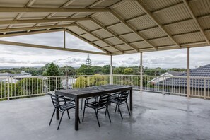 Ein überdachter Außenbereich mit Tisch und Stühlen, einem Metallgeländer und Blick auf Gebäude und Bäume.
